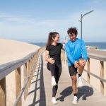 A young couple doing warm-up exercises on a boardwalk by the beach, enjoying a healthy lifestyle outdoors.